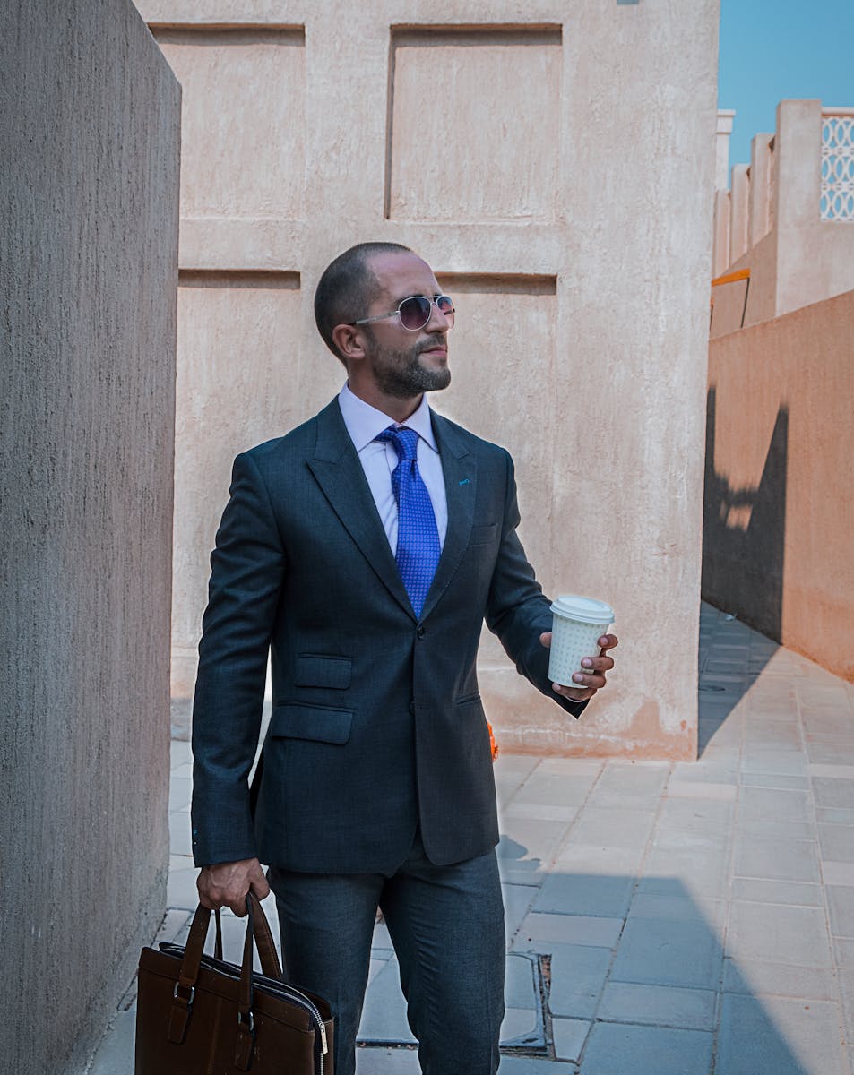 Professional businessman in a suit, holding coffee, walking outdoors in Dubai.