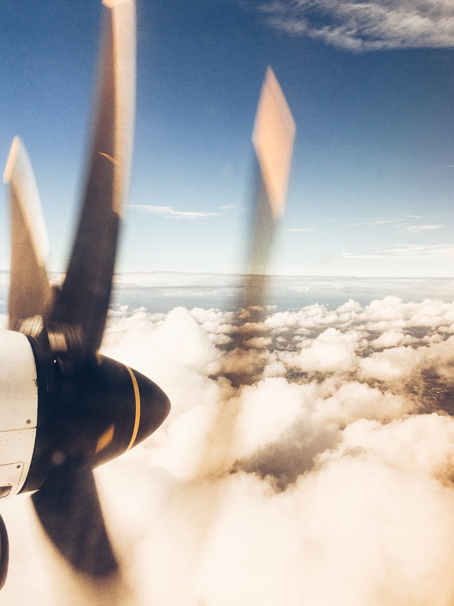 Dynamic view of an airplane propeller with fluffy clouds over a serene sky.