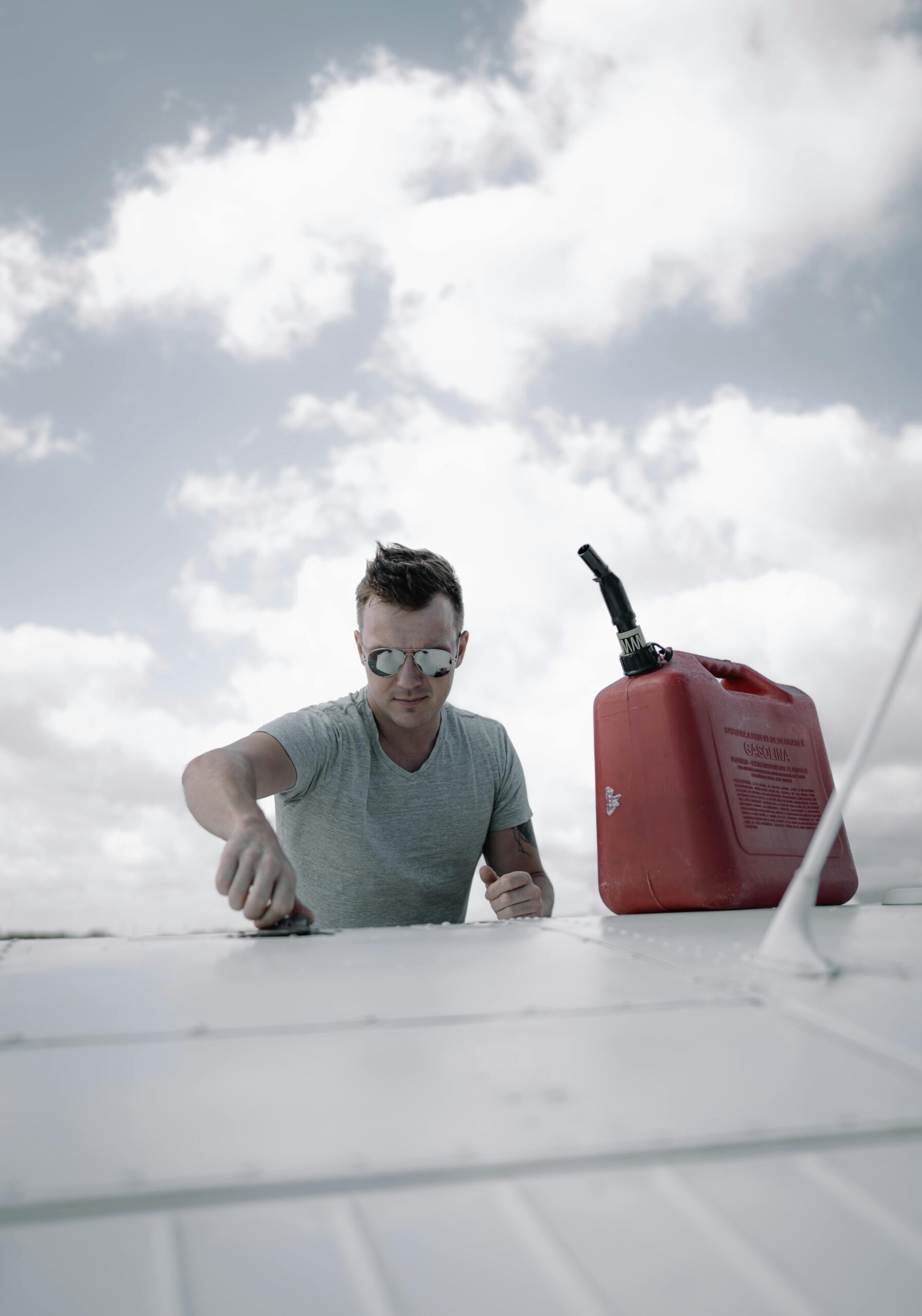 Young concentrated male mechanic in casual clothes and sunglasses pouring fuel into airplane tank before flight